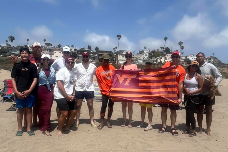 LA Hokies pose at the beach with a giant Virginia Tech flag